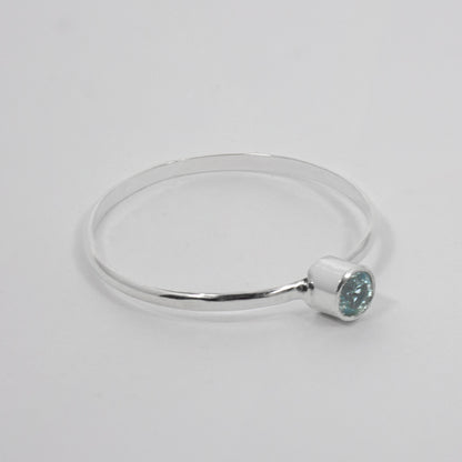 Sterling silver ring featuring a dainty blue topaz solitaire gemstone in a tube setting, elegant jewelry piece by Grey Clymene.