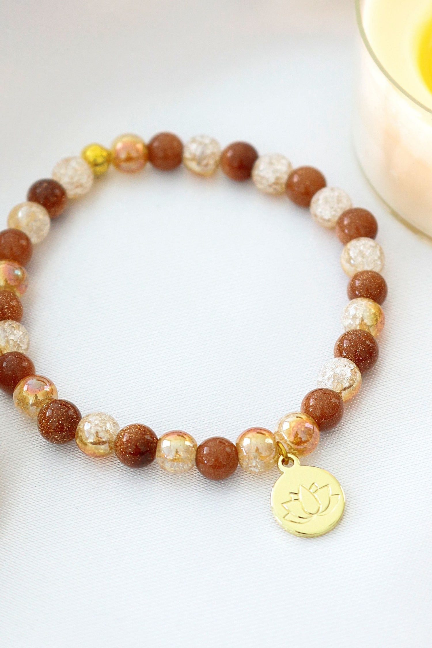 Goldstone elastic bracelet with a 24K gold lotus flower charm, featuring a sleek design and vibrant gemstone beads.