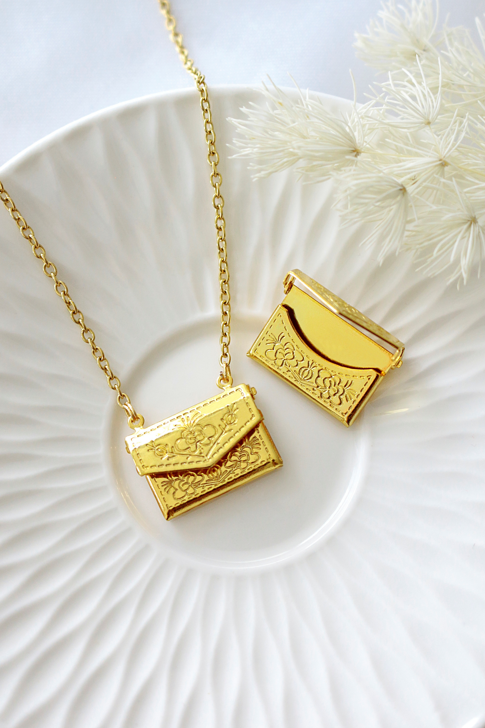 Ultramarine Birch 24 Karats Daisy Envelope Locket Necklace with gold-tone floral design on a chain, close-up view.