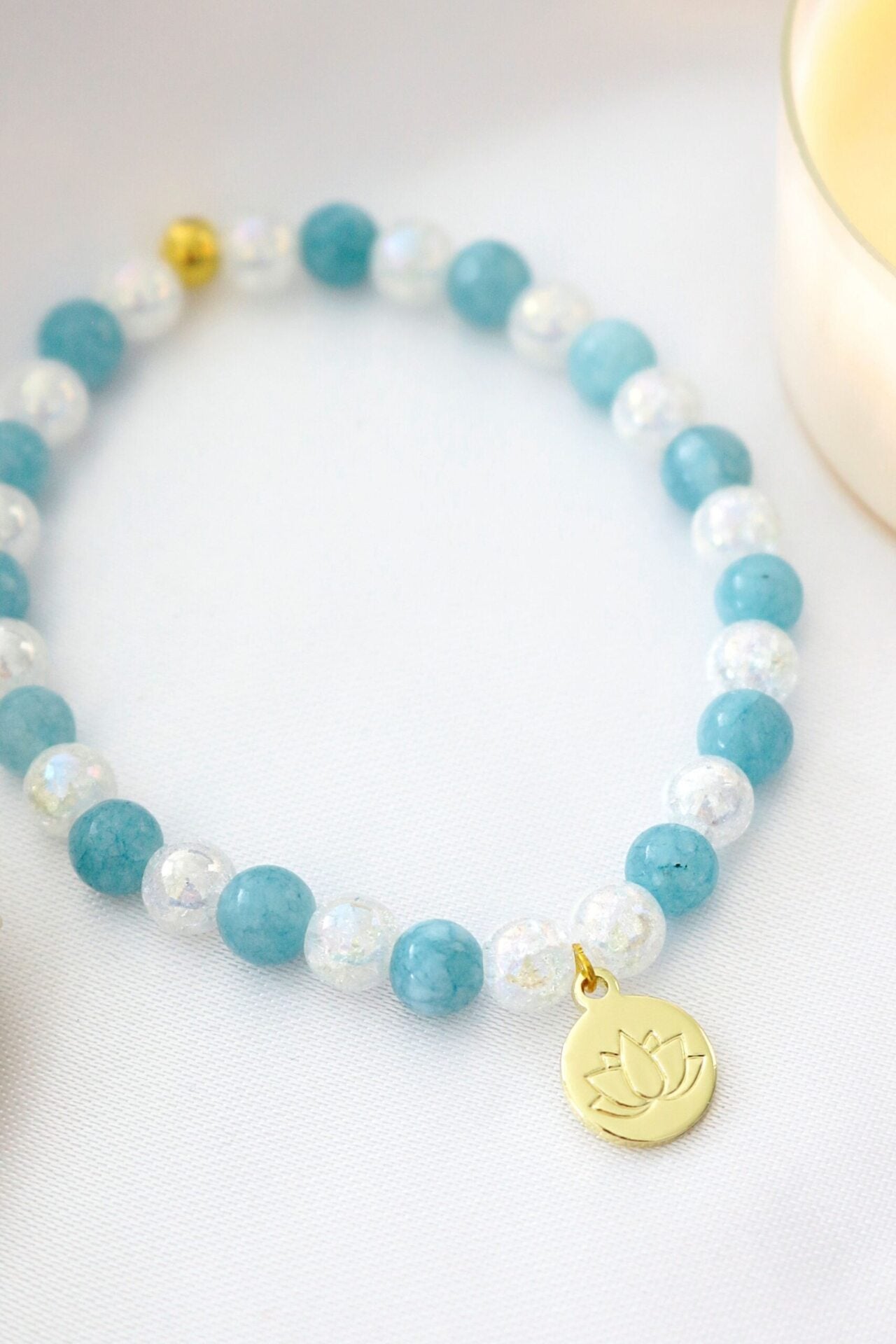 Ultramarine Birch aquamarine elastic bracelet with a 24K gold lotus flower charm, featuring smooth blue beads and delicate gold accents.