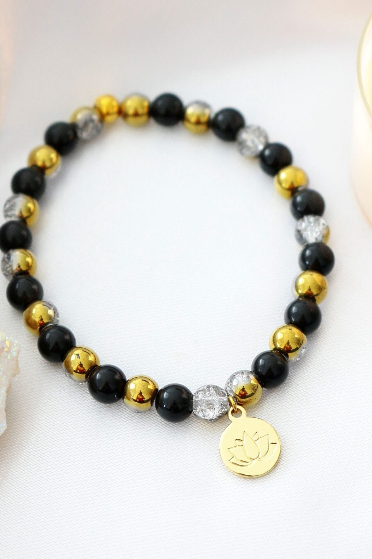 Black obsidian elastic bracelet with a gold lotus flower charm by Ultramarine Birch, featuring stretchable design and polished stones.