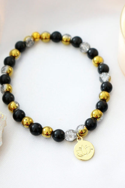 Black obsidian elastic bracelet with a gold lotus flower charm by Ultramarine Birch, featuring stretchable design and polished stones.