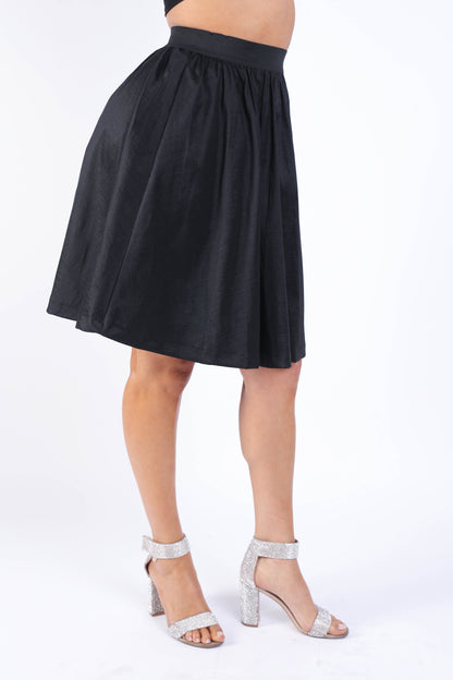 Black pleated midi flare skirt with high waist and casual elastic waistband by Puce Juniper, shown on a model.