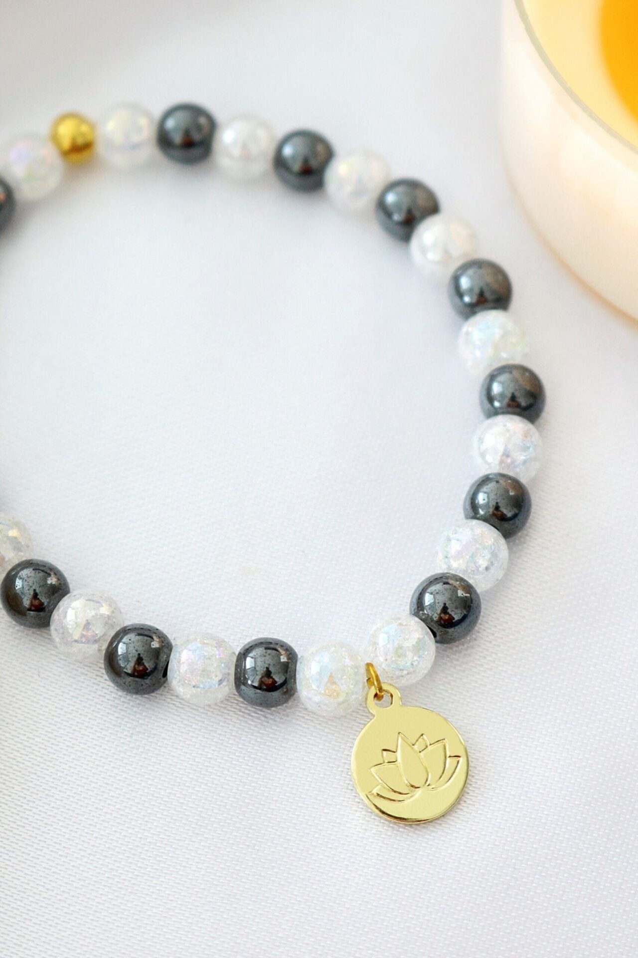 Hematite elastic bracelet with a gold lotus flower charm, featuring sleek black beads and a subtle metallic sheen.