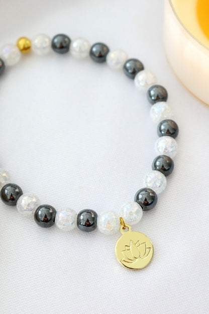 Hematite elastic bracelet with a gold lotus flower charm, featuring sleek black beads and a subtle metallic sheen.