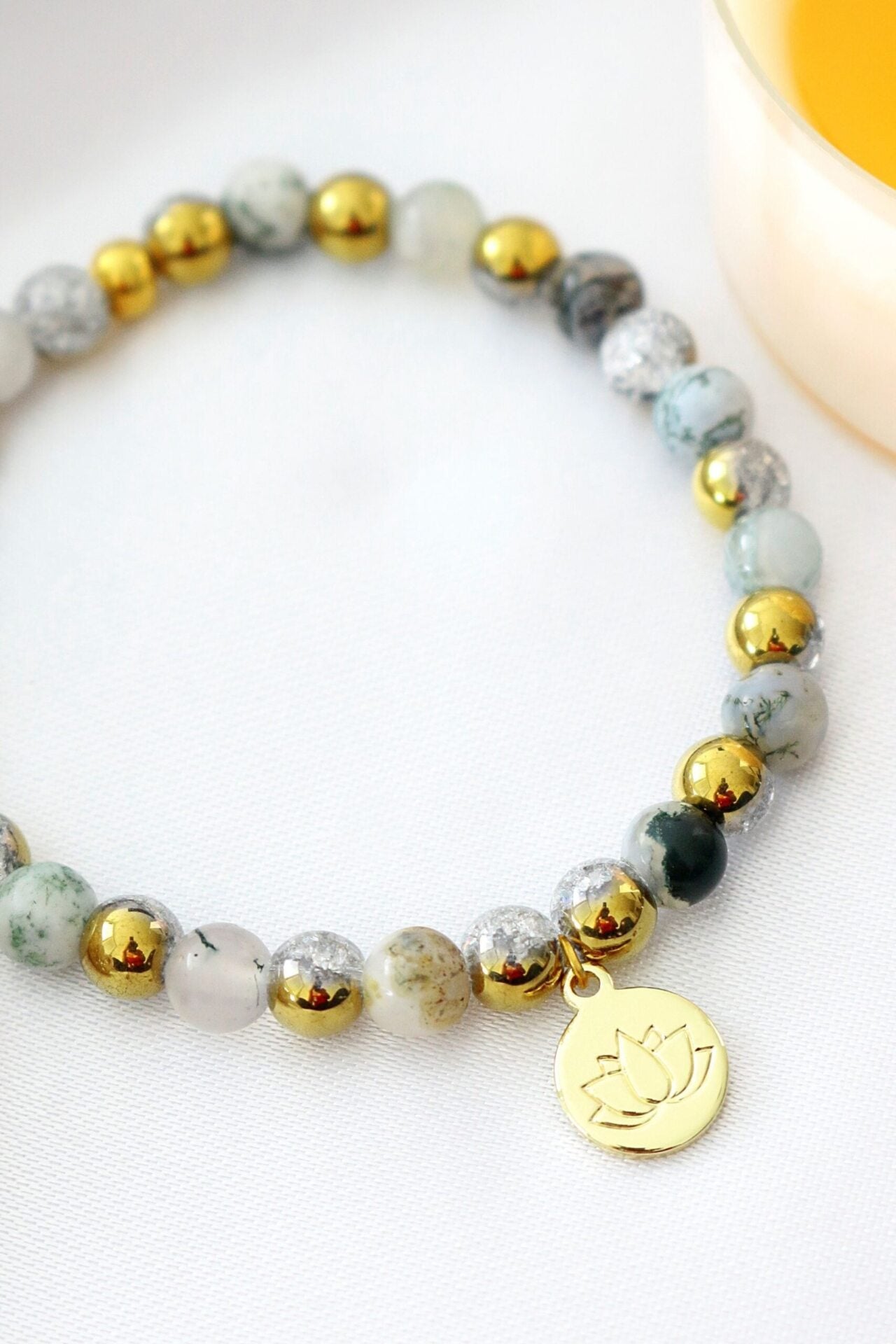 Mossy agate elastic bracelet with 24K gold lotus flower charm, featuring natural stone beads and a stylish, handcrafted design.