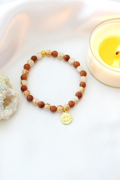 Goldstone elastic bracelet by Ultramarine Birch with a 24K lotus flower charm and smooth goldstone beads.