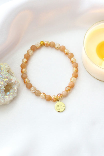 Sunstone elastic bracelet with 24K lotus flower charm by Ultramarine Birch, featuring vibrant orange sunstone beads and a gold lotus pendant.