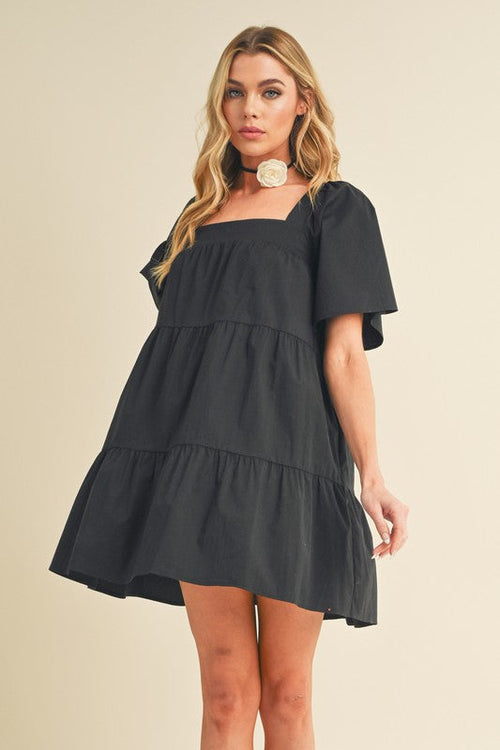 A woman wearing the Jade Icarus Aemi + Co square neck half sleeve tiered dress, showcasing its layered skirt and fitted bodice.