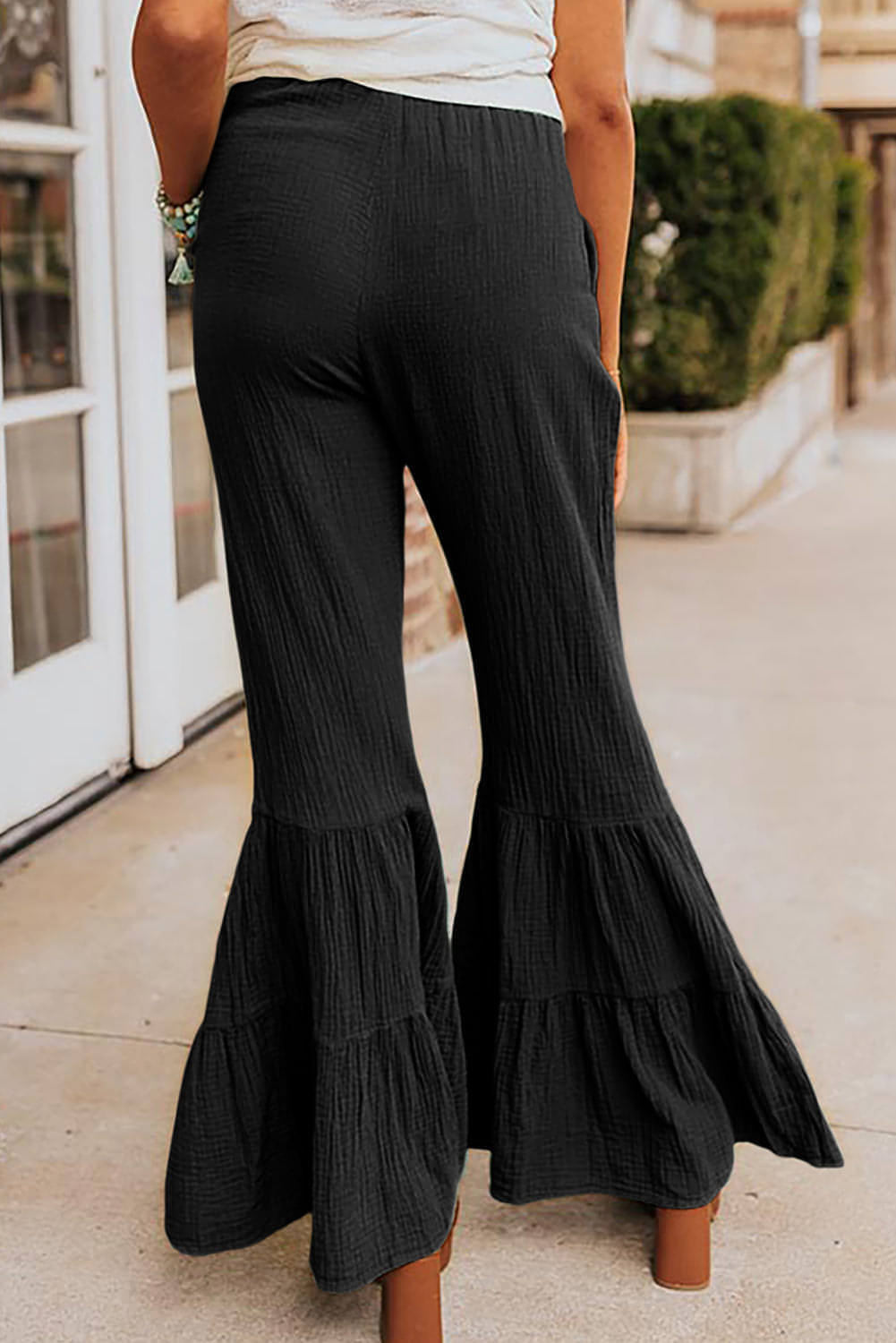 Black textured high waist ruffled bell bottom pants by Carmine Juneberry, showing detailed fabric texture and flared design.