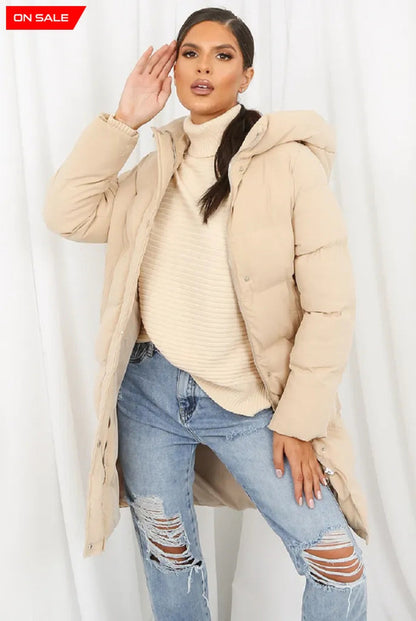 Beige hooded longline puffer coat by Rose Eleusis, featuring a cozy, insulated design with a front zipper and oversized fit.