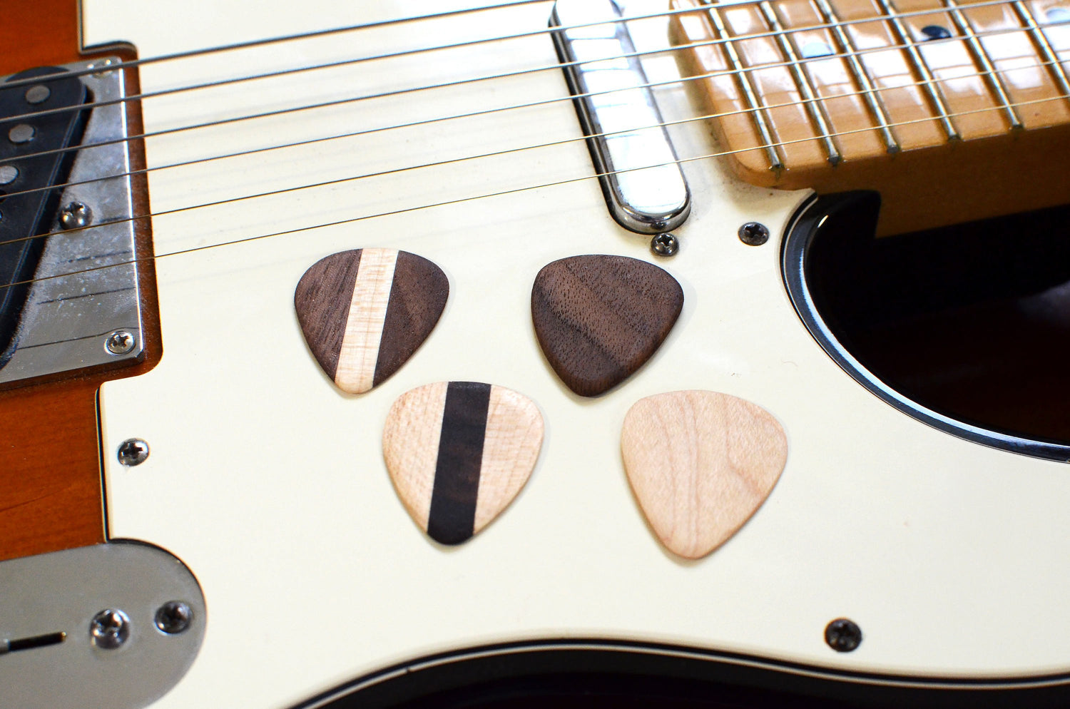 Set of four hardwood guitar picks by Pinwheel, showing different natural wood grain patterns on a plain background.