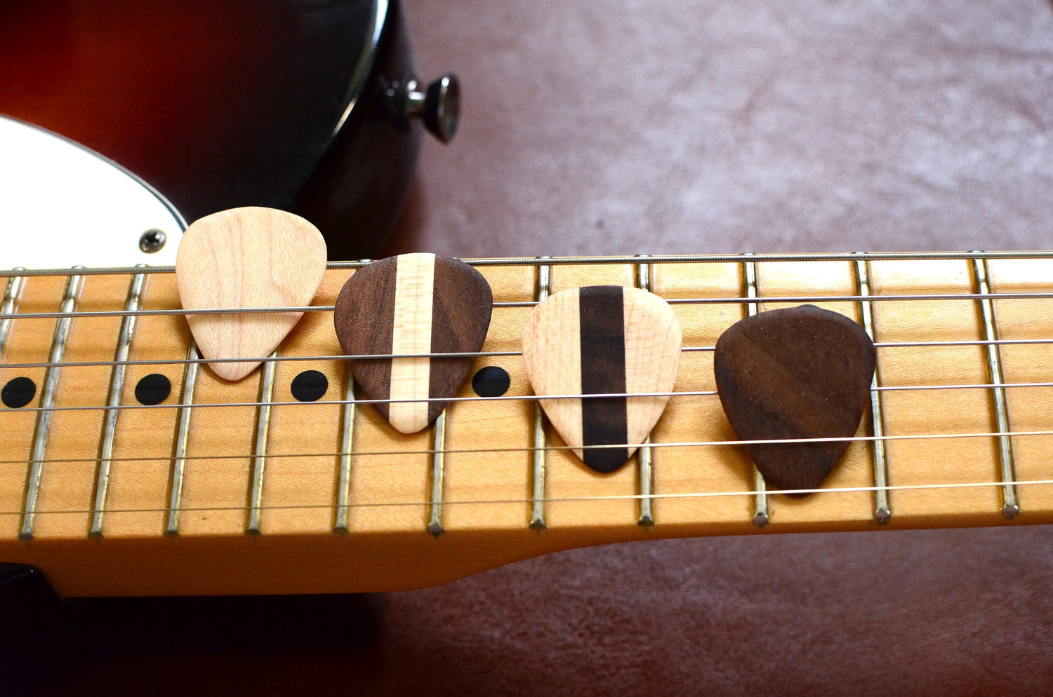 Set of four hardwood guitar picks by Pinwheel, showing textured natural wood surfaces for musical instrument playing.