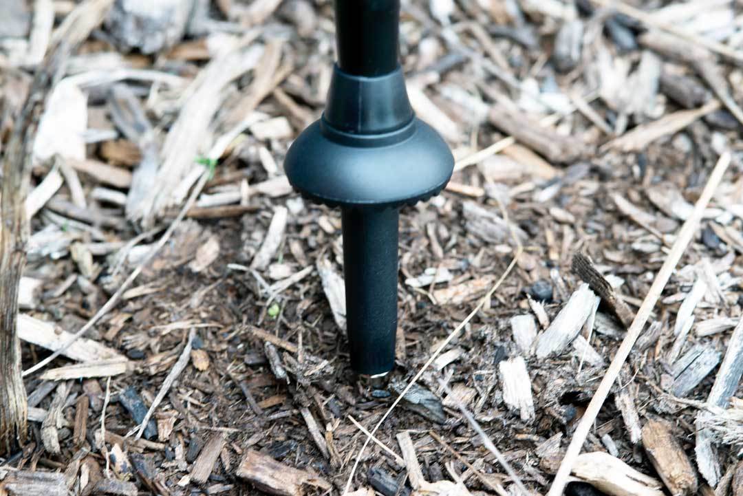 Triangulum trekking poles with universal carbide tips and compact baskets, shown on a bed of wood chips during a camping hike.