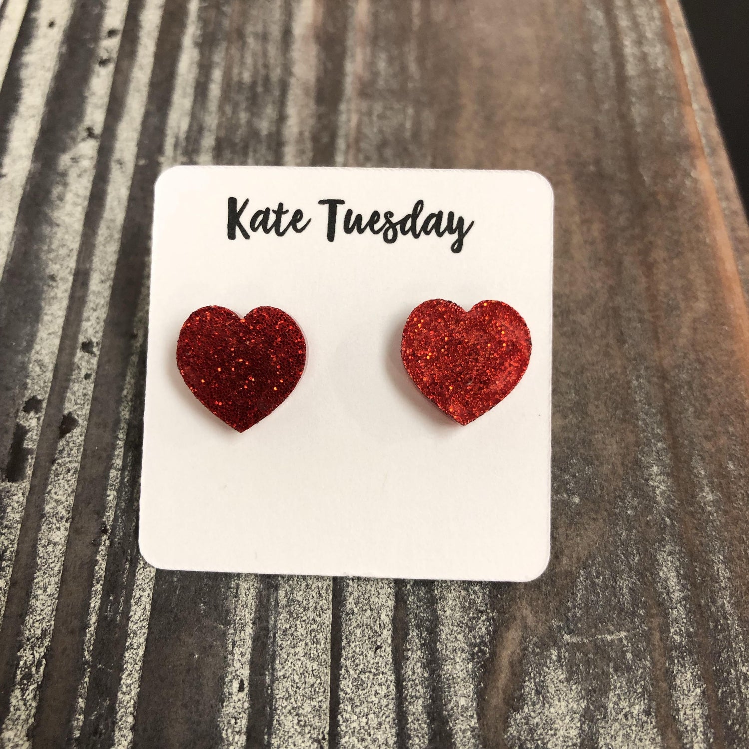 Red glitter heart stud earrings from Olive Felix, close-up view showing shiny heart-shaped earrings with sparkling glitter finish.